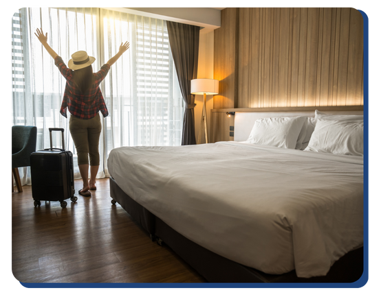 Female guest entering a brightly lit, freshly cleaned hotel room with arms raised in excitement, showcasing a welcoming and pristine hospitality experience.