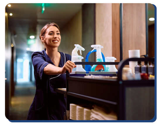 Smiling hotel housekeeper pushing a fully stocked cleaning cart down a hallway, highlighting readiness and professionalism in cleaning operations.