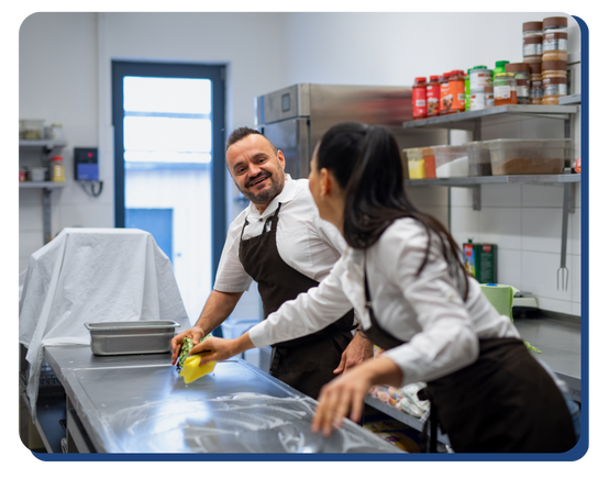 Two retail kitchen employees scrubbing a stainless steel countertop, ensuring sanitary conditions through thorough commercial cleaning services.
