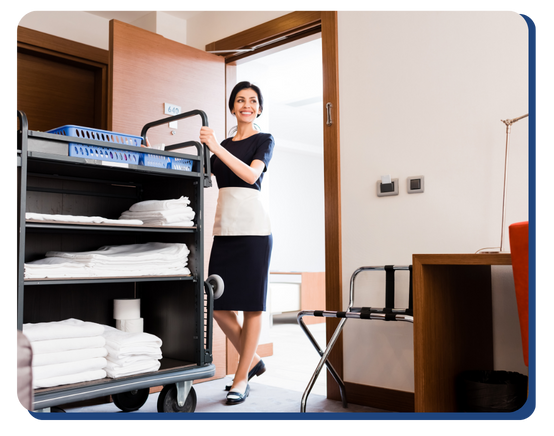 Smiling hotel housekeeper entering a guest room with a fully stocked linen cart, ready to perform cleaning and replenishment duties.