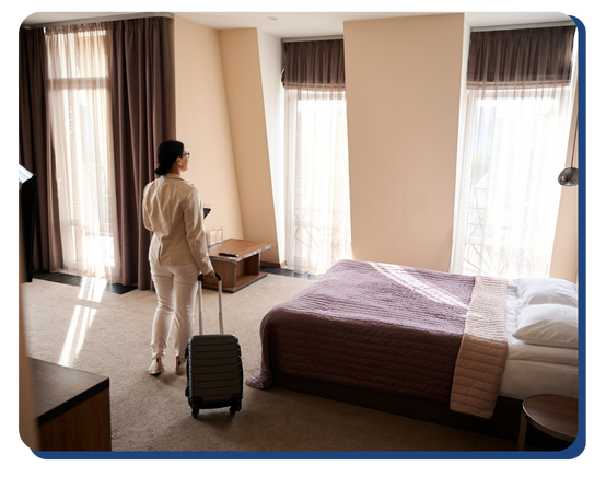 Female guest arriving with suitcase into a freshly cleaned, sunlit hotel room with a made bed and tidy modern furnishings, reflecting high housekeeping standards.