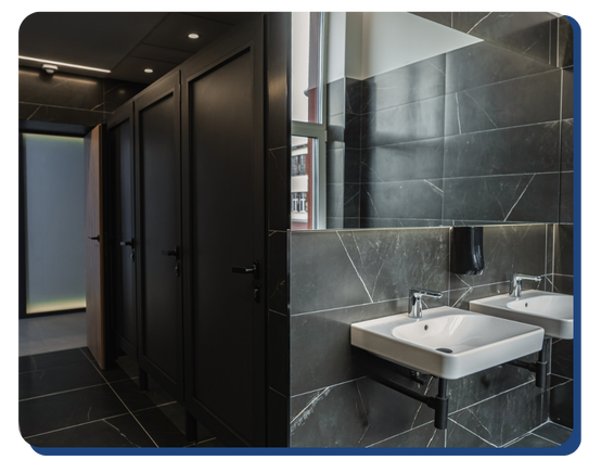 Stylish public restroom with black tiled walls and floors, two sinks, and multiple closed stalls, showcasing a professionally cleaned modern facility.