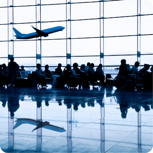 Silhouettes of people sitting and waiting in an airport terminal with large windows, as a plane takes off outside. The scene is reflected on the shiny floor.