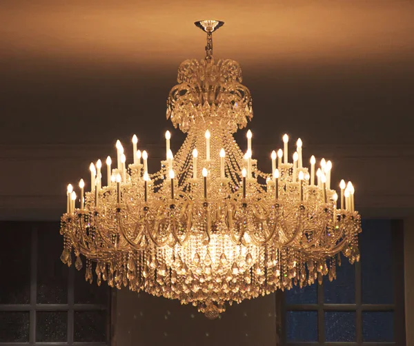 A large, ornate crystal chandelier with multiple tiers and numerous lit candle-shaped bulbs hangs from the ceiling, casting a warm glow in the room—an ideal setting for Impact Commercial Cleaning Services in Canada.
