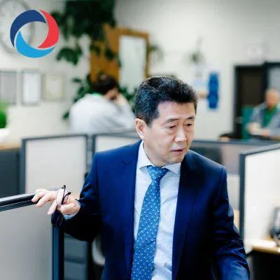 A man in a blue suit and tie stands in an office holding his glasses, with cubicles and colleagues visible in the background. A circular logo hints at impact commercial cleaning services on the wall, reflecting a professional workspace in Canada.