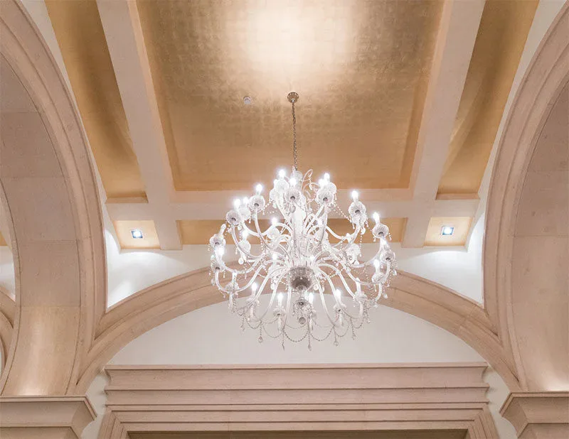 A crystal chandelier hangs from a gold-accented coffered ceiling with arched architectural details and recessed lighting, showcasing the refined ambiance maintained by impact commercial cleaning services.