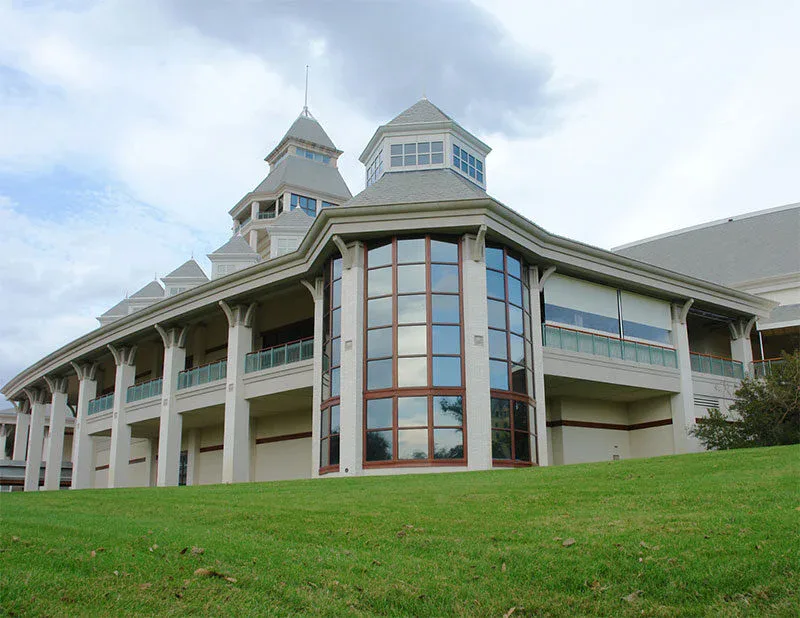 A large building with tall glass windows, white columns, and multiple peaked roofs sits on a grassy hill under a cloudy sky, reflecting the high standards set by impact commercial cleaning services in Canada.