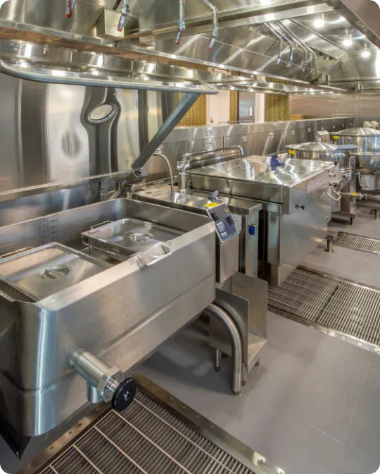A modern, industrial kitchen with stainless steel appliances, deep sinks, and cooking stations, all neatly arranged in a clean, professional environment.