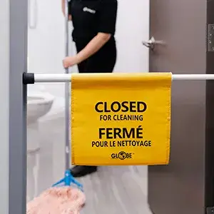 A yellow sign reading Closed for cleaning in English and French hangs on a restroom door, while a person from impact commercial cleaning services mops the floor inside.