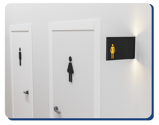 Two white restroom doors are shown side by side. One door has a male symbol; the other has a female symbol. A black sign with a yellow female icon is mounted on the wall above the door with the female symbol.
