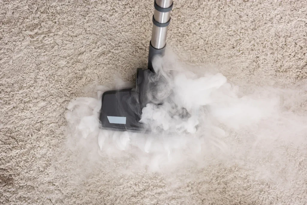 A steam cleaner emits visible steam while cleaning a light-colored carpet, showcasing the effectiveness of impact commercial cleaning services as the cleaning head moves across the surface.