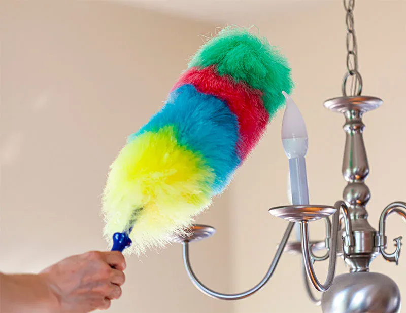 A hand uses a colorful duster with green, red, blue, and yellow sections to clean a silver chandelier—illustrating the attention to detail provided by impact commercial cleaning services.